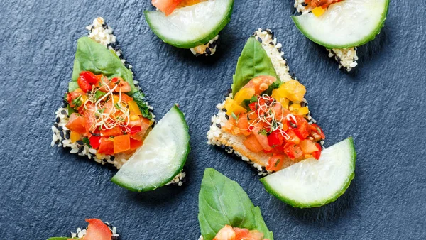 Appetizer canape with chopped vegetables and sesame on stone slate background close up. Delicious snacks, sandwiches, crostini, bruschetta, antipasti on party or picnic time. Top view