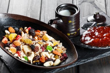 Müsli kase yoğurt, granola, dilimlenmiş muz, kaju fıstığı, badem, kızılcık, fındık, Kuru meyveler ile koyu ahşap masa, closeup görünümü karıştırın. Sağlıklı kahvaltı kase yemek. Vejetaryen yiyecekler kavramı