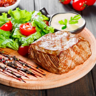 Izgara biftek domuz eti taze sebze salatası, domates ve ahşap kesme tahtası üzerinde sos ile.