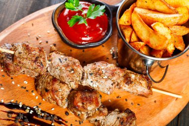 Et şiş ahşap kesme tahtası üzerine bir kova içinde sos ve patates kızartması ile.