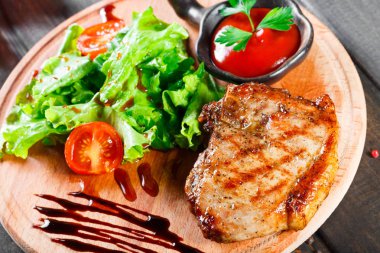 Izgara biftek domuz taze sebze salatası, domates ve ahşap kesme tahtası üzerinde sos ile. Sıcak et yemekleri. Üstten görünüm.