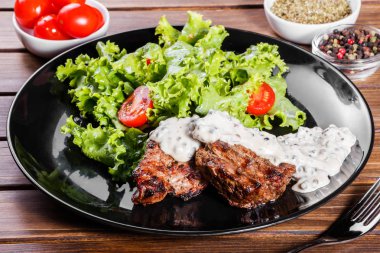 Izgara et taze sebze salata ve domates siyah plaka, ahşap arka plan ile. Sıcak et yemekleri.