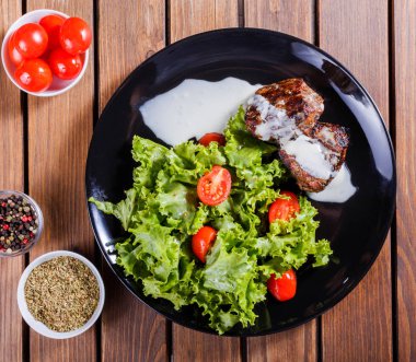 Beaf biftek et taze sebze salatası ve siyah plaka, ahşap arka plan üzerinde domates ızgara. Sıcak et yemekleri.