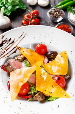 Sığır eti biftek chargrilled Orta nadir kiraz domates, mantar ve peynir koyu ahşap zemin üzerine sıcak salata. Sıcak et yemekleri. Maddeler tablosundaki. Üstten görünüm