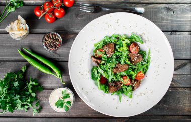 Sıcak kızarmış karaciğer, kiraz domates ve koyu ahşap zemin üzerine karışık yeşillik salatası. Sağlıklı gıda. Maddeler tablosundaki. Üstten görünüm