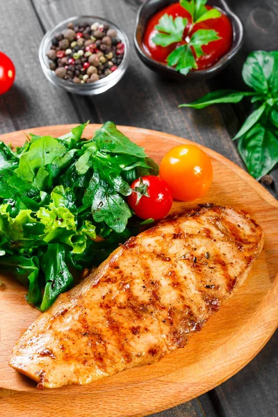 Grilled chicken fillet with fresh vegetable salad, tomatoes and sauce on wooden cutting board.
