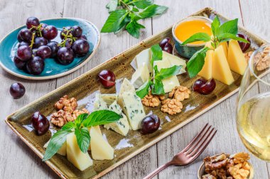 Tatlım, ceviz, üzüm, ekmek, nane ve şarap ile süslenmiş ahşap arka plan üzerinde peynir tabağı. Aperatifler ve şarap meze seti