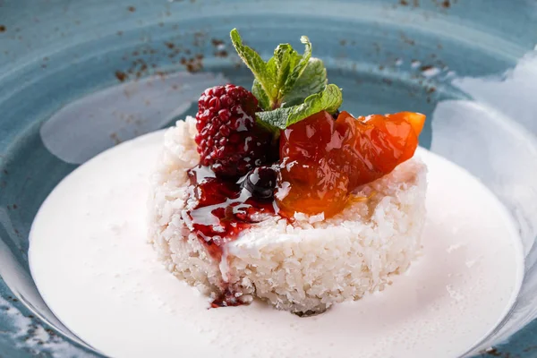 Rice porridge with coconut milk, fruit jam, berries and mint on plate. Top view on a dark grey stone surface. Healthy breakfast, vegan food. Top view