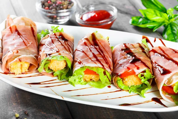 Fried meat wrapped in a prosciutto with tomatoes on wooden background. Hot Meat Dishes. Top view.
