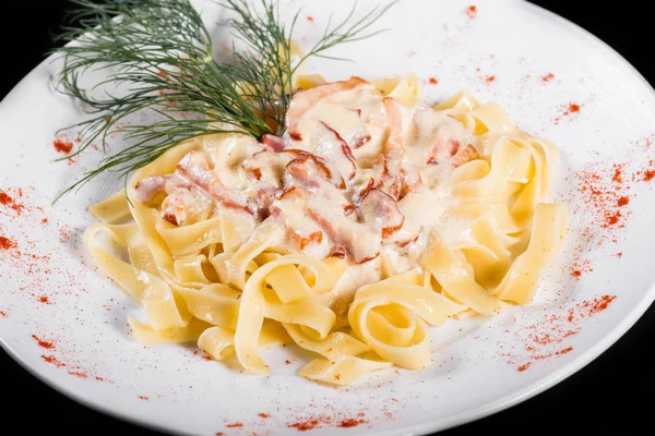 Fettuccine pasta with meat, cream sauce and herbs, in bowl isolated on black background. Italian cuisine.