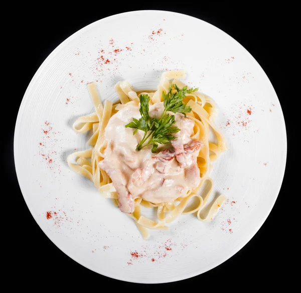 Fettuccine pasta with meat, cream sauce and herbs, in bowl isolated on black background. Italian cuisine. Top view.