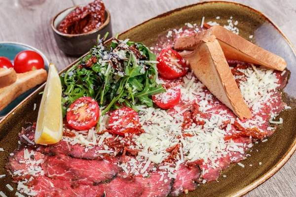 Meat Carpaccio with Rocket Salad, Parmesan Cheese, tomatoes on light wooden background. Snacks and Wine appetizers set. Ingredients on table. Top view