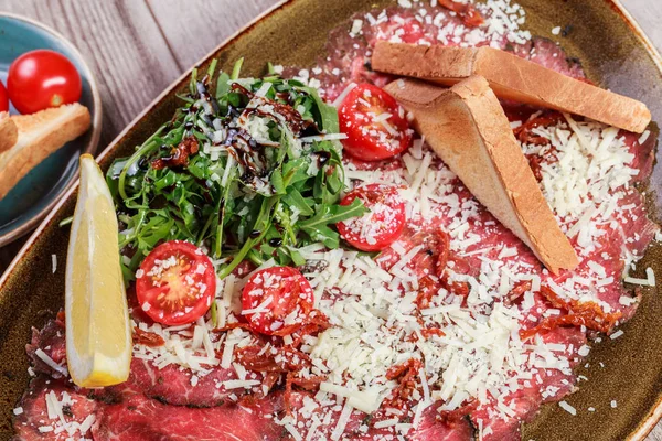 Hafif ahşap zemin üzerine roket salata, Parmesan peyniri, domates et Carpaccio. Aperatifler ve şarap meze ayarlayın. Maddeler tablosundaki. Üstten görünüm