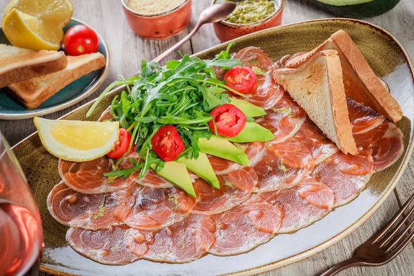 Salmon Carpaccio with Rocket Salad, avocado, tomatoes, lemon on light wooden background. Snacks and Wine appetizers set. Ingredients on table. Top view