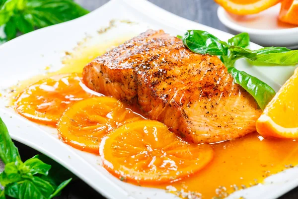 Portakal dilimleri, baharat ve koyu arka plan üzerinde beyaz tabakta fesleğen ile Glazed fileto somon tatlım. Lezzetli yemek deniz ürünleri.