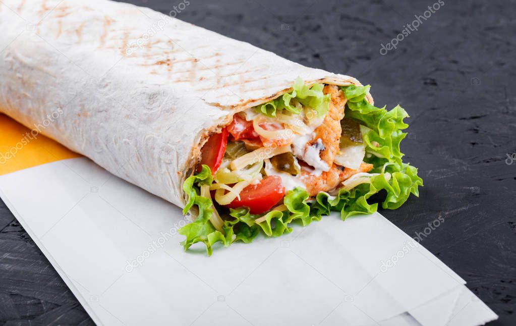 Burrito wraps from fillet grilled chicken, lettuce, slices of fresh tomatoes, pickles and cheese on dark wooden background. Healthy lunch