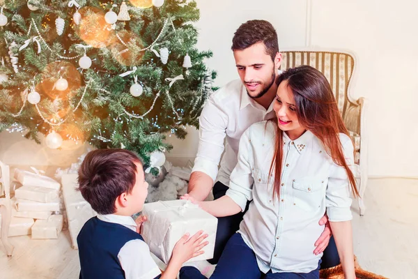Happy family give gifts in the living room, behind the decorated Christmas tree, the light give a cozy atmosphere. New Year and xmas theme