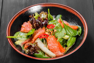 Yaprak sebze salatası somon füme, ıspanak, biber, salatalık ve koyu ahşap arka plan üzerinde plaka üzerinde sos ile. Akdeniz yemekleri. Üstten görünüm