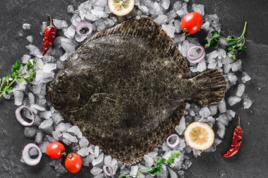 Raw whole flounder fish with spices on ice over dark stone background. Creative layout made of fish, top view clipart