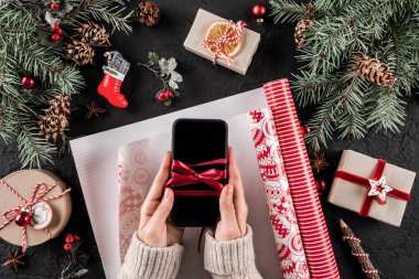 Erkek bir Noel hediyesi, telefon tatil çam dalları, kırmızı süslemeleri siyah zemin üzerine sarma kaydırma eller. Noel ve mutlu yeni yıl kartı. Düz yatıyordu, en iyi görünümü