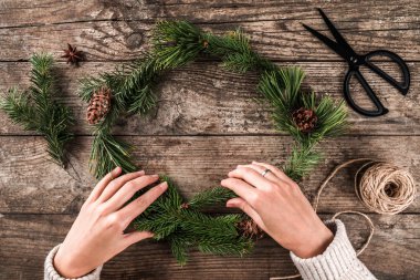 Eller kadın Noel çelenk çam dalları ve çam kozalakları ahşap arka plan üzerinde yapım makas ve Jüt skein. Noel ve mutlu yeni yıl kartı. Düz yatıyordu, en iyi görünümü