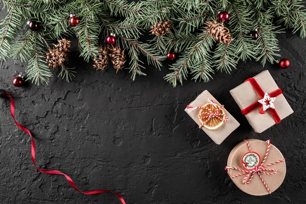 創造的なレイアウトは クリスマス ツリーの枝 ギフト 暗い背景に赤いリボンのマツ円錐形から成っています クリスマスと新年のテーマです フラット レイアウトのトップ ビューでテキストのためのスペース — ストック写真