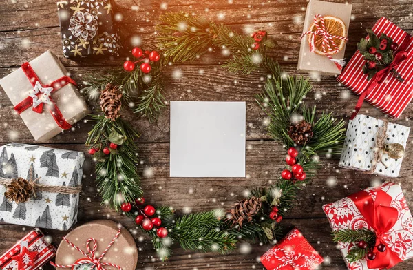 Noel çelenk çam dalları, birçok Noel hediye kutuları kırmızı dekorasyon, kartı ve çam kozalakları kar taneleri ile ahşap arka plan üzerinde. Noel ve mutlu yeni yıl tema. Düz yatıyordu, en iyi görünümü