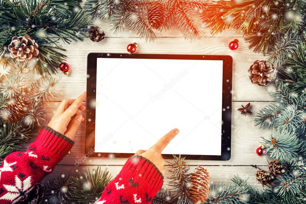 Hands using the tablet pc on Christmas background with fir branches, pine cones, balls. Xmas and New Year theme. Flat lay, top view, space for text