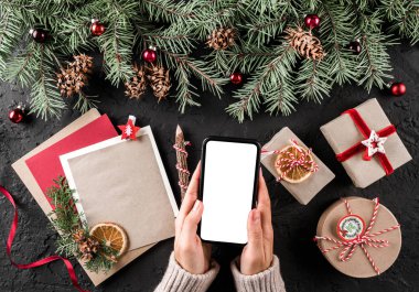 Cep telefonu tutan eller. Noel hediye kutuları kırmızı dekorasyon, çam dalları, çam kozalakları tatil arka plan üzerinde. Noel ve mutlu yeni yıl kartı. Düz yatıyordu, en iyi görünümü