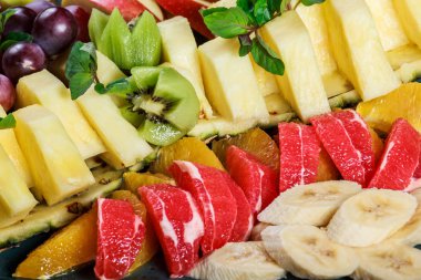 Plaka üzerinde çeşitli taze meyve. Elma, üzüm, kivi, ananas, greyfurt, portakal, muz ve nane ahşap masa üzerinde. Seçici odak
