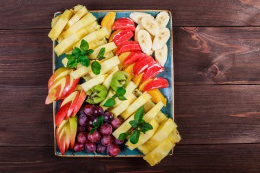 Plaka üzerinde çeşitli taze meyve. Elma, üzüm, kivi, ananas, greyfurt, portakal, muz ve nane ahşap masa üzerinde. Üstten görünüm