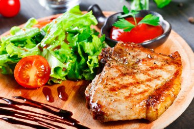 Izgara biftek domuz taze sebze salatası, domates ve ahşap kesme tahtası üzerinde sos ile. Sıcak et yemekleri. Üstten görünüm