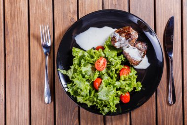 Beaf biftek et taze sebze salatası ve siyah plaka, ahşap arka plan üzerinde domates ızgara. Sıcak et yemekleri