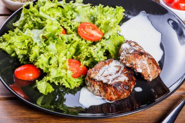 Beaf biftek et taze sebze salatası ve siyah plaka, ahşap arka plan üzerinde domates ızgara. Sıcak et yemekleri