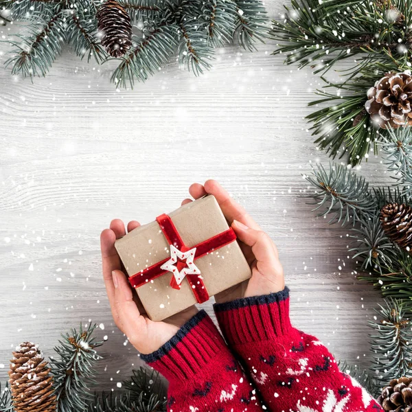 女性手拿着圣诞礼品盒在白色木背景与冷杉分枝 圣诞节和新年快乐的主题 平面布局 顶部视图 — 图库照片