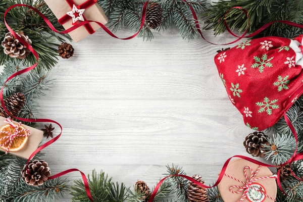 Yaratıcı düzen çerçeve yaptı Noel ağaç dalları, kağıt kartı Not, çam kozalakları, hediyeler, Noel Çanta Beyaz ahşap zemin üzerinde. Noel ve yeni yıl tema. Düz yatıyordu, en iyi görünümü