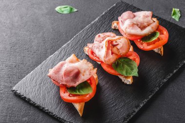 Meze bruschetta salam, jambon, domates ve baharat siyah şeyl üzerinde siyah taş zemin kurulu. Sağlıklı gıda kavramı