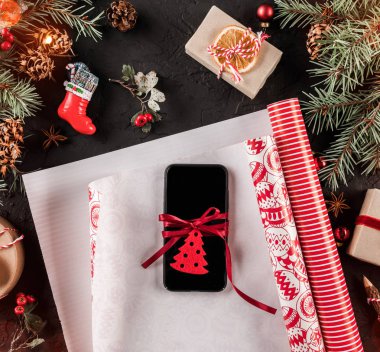Cep telefonu, xmas kaydırma, çam dalları, hediyeler, koyu arka plan üzerinde kırmızı süslemeleri ile Noel kompozisyon. Noel ve mutlu yeni yıl kartı, bokeh, kıvılcım, parlayan. Düz yatıyordu, en iyi görünümü