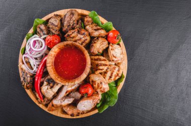 Çeşitli lezzetli ızgara et ve sosis domates ve kesme tahtası siyah taş zemin üzerine Barbekü sosu ile. Sıcak et yemekleri. Üstten görünüm, düz yatıyordu