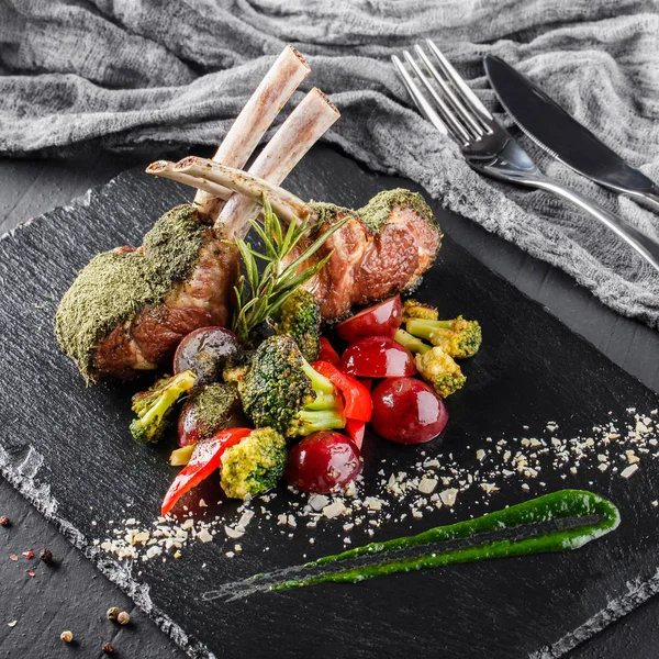 Tomahawk rib beef steak on bone and vegetables with sauce on black shale board over black stone background. Hot Meat Dishes