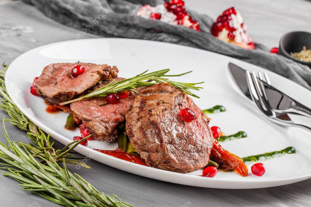 Juicy medium beef fillet steaks mignon with green beans, pomegranate and sauce in plate on grey background. Hot Meat Dishes, top view