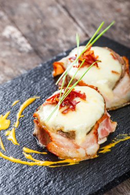 Ahşap arka plan üzerinde taş arduvaz arka plan üzerinde kurutulmuş domates Dana biftek, peynirli jambon sarılı kapatalım. Sıcak et yemekleri. Üstten görünüm 