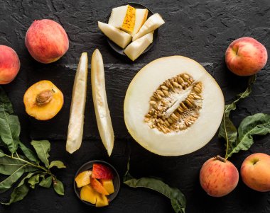 Kavun ve şeftaliler. Meyve yapılmış yaratıcı düzeni. Siyah taş zemin üzerine renkli taze meyve. Üstten görünüm, düz yatıyordu