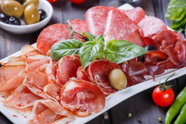 Meze tabağı soğuk et tabağı prosciutto, dilim jambon, salam, zeytin ahşap zemin üzerinde ve fesleğen ile dekore edilmiştir. Etli meze. Üstten görünüm