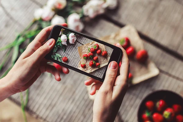 Girl\'s hands taking photo of breakfast with strawberries by smartphone. Healthy breakfast, Clean eating, vegan food concept. Top view