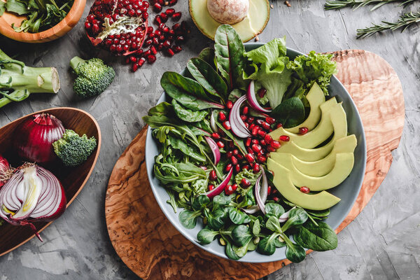 Healthy fresh salad with avocado, greens, arugula, spinach, pomegranate in plate over grey background. Healthy vegan food, clean eating, dieting, top view