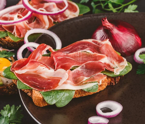 Täysjyväleipää Voileipiä Prosciutto Avokado Kurkku Tomaatit Yrtit Siemenet Lautasella Musta — kuvapankkivalokuva