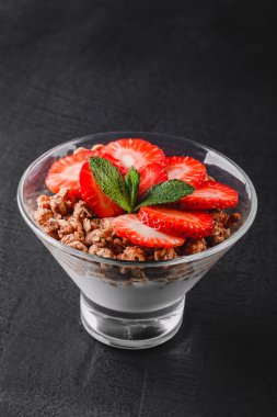 Lezzetli granola yoğurt ve cam siyah arka plan üzerine taze çilek ile. Sağlıklı kahvaltı malzemeler. Yeme, vegan gıda kavramı temiz. Üstten görünüm