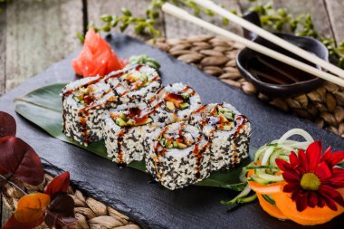 Suşi kara taş üzerine bambu hasır, seçici odak üzerinde set karides tempura, salatalık, avokado ve susam ile alır. Japon mutfağı