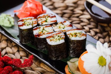 Suşi Roll - Maki Sushi füme yılan balığı, salatalık ve avokado çiçeklerle süslenmiş bambu mat siyah taş. Japon mutfağı